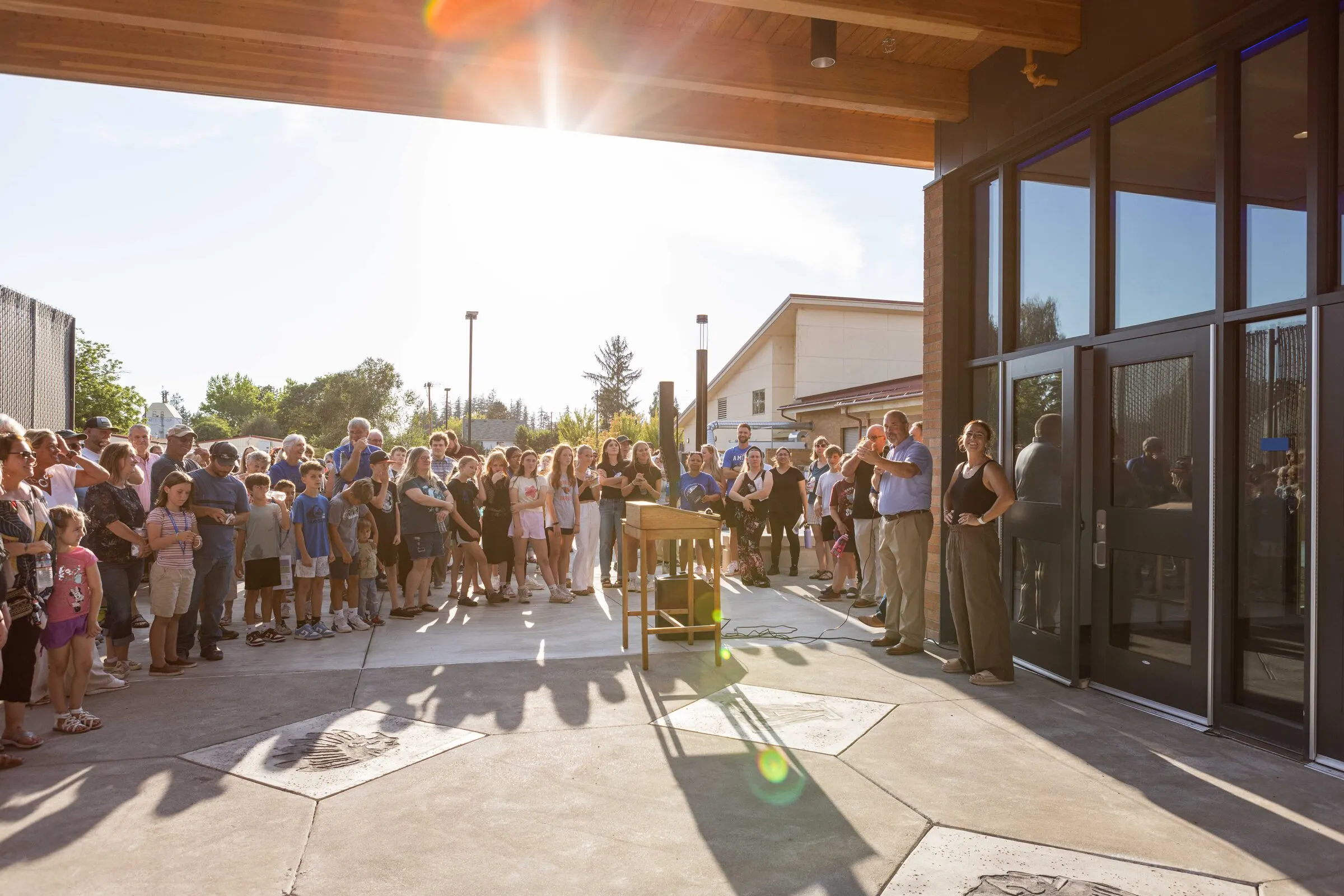 Amity community gathered outside the new school entrance at the opening ceremony, families and students filling the covered walkway in the afternoon sun.