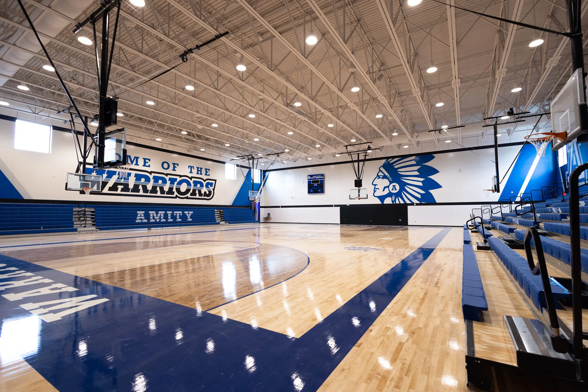 The gym, with "Home of the Warriors" painted on the wall above blue bleachers.